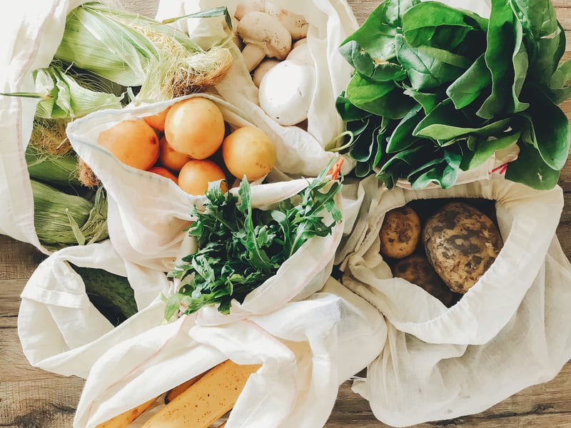 fresh vegetables in eco cotton bags on table in the kitchen. lettuce, corn, potatoes, apricots, bananas, rucola, mushrooms from market. zero waste shopping concept. ban plastic